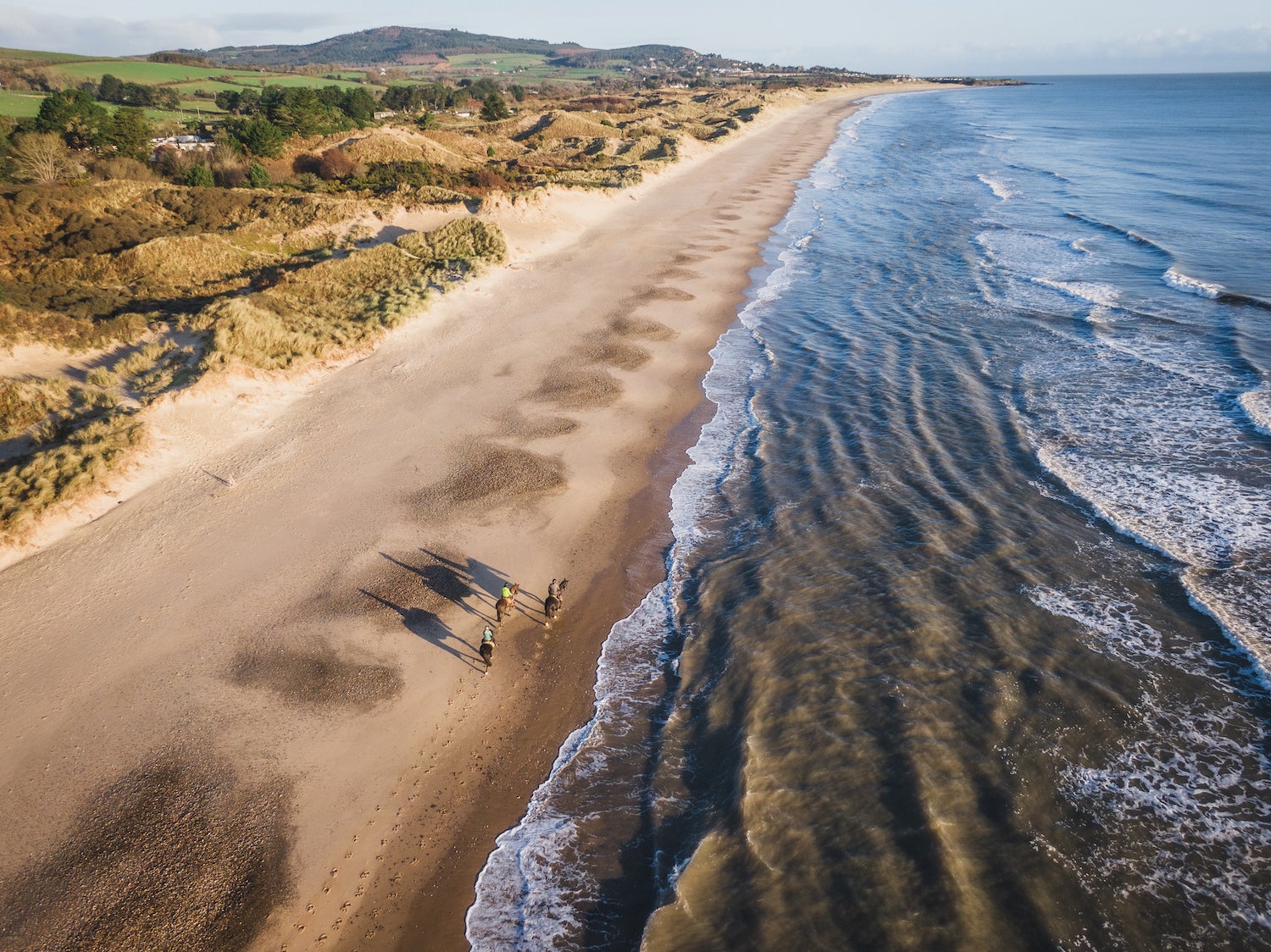Aerial shot of three people horse riding on Brittas Bay beach in County Wicklow.