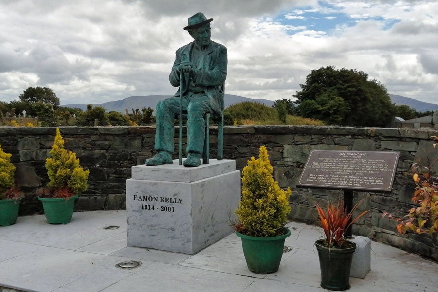 Bronze life sized seated statue of Eamon Kelly in a storytelling pose on a marble plinth