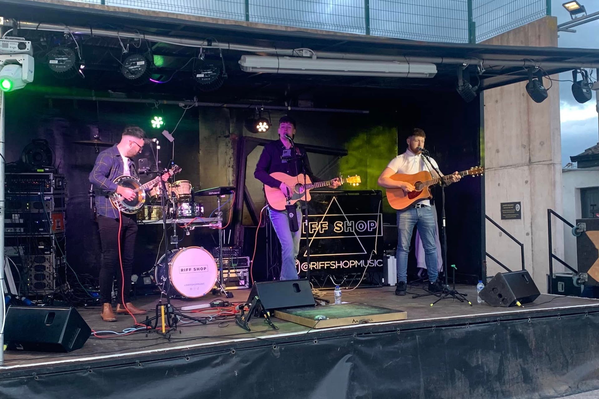 3 men playing guitar in a band on a small stage outdoors.