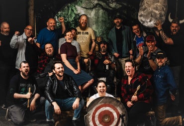 Group of smiling people holding axes and standing behind a target board