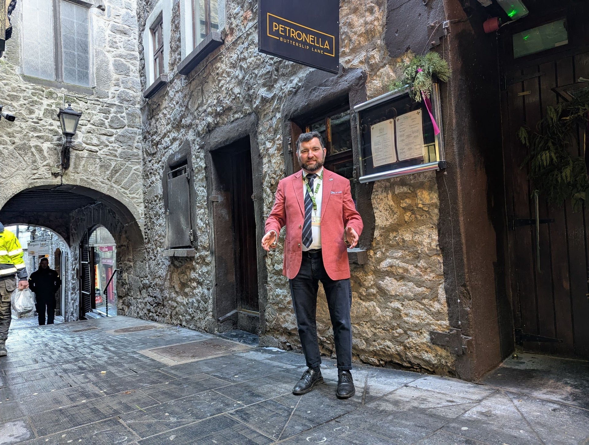 A tour guide in a pink jacket stands in a medieval laneway