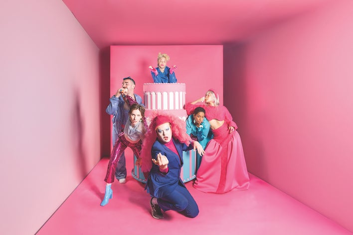 A small, narrowing pink room with people in various poses dressed in shades of pink and blue.