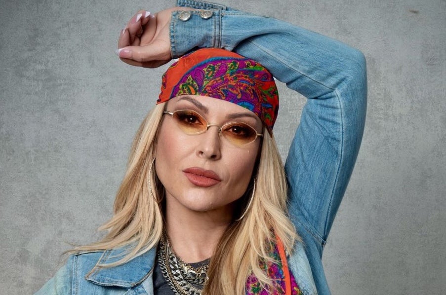 Pop icon Anastacia, a woman wearing small sunglasses and a headscarf with her left arm resting on the top of her head.
