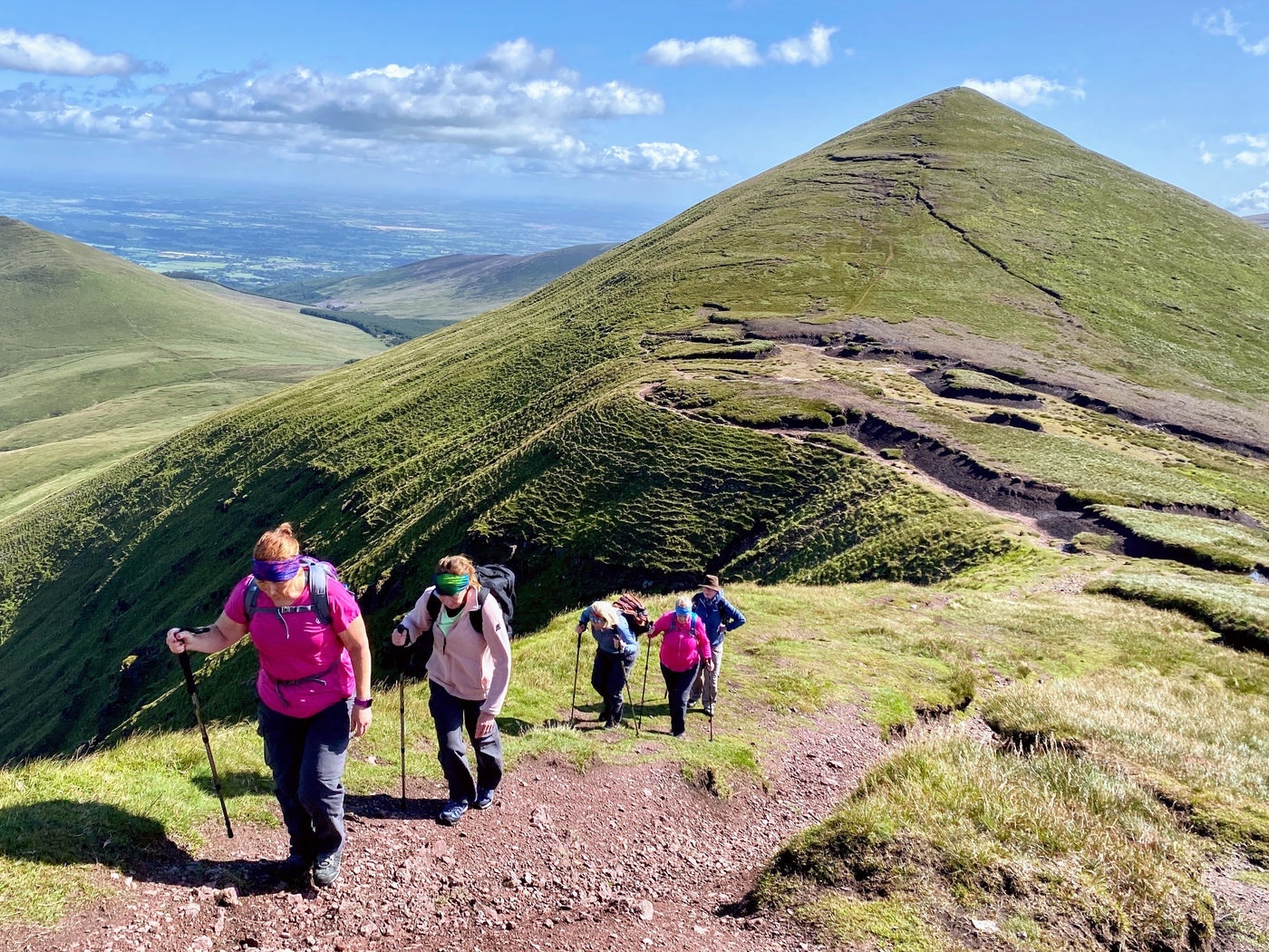 A group of hikers walking up a mountain path with another mountain in the background