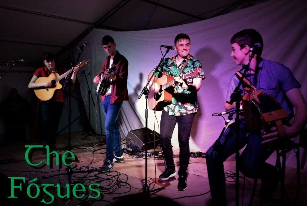 4 men on a small stage playing guitars and smiling.