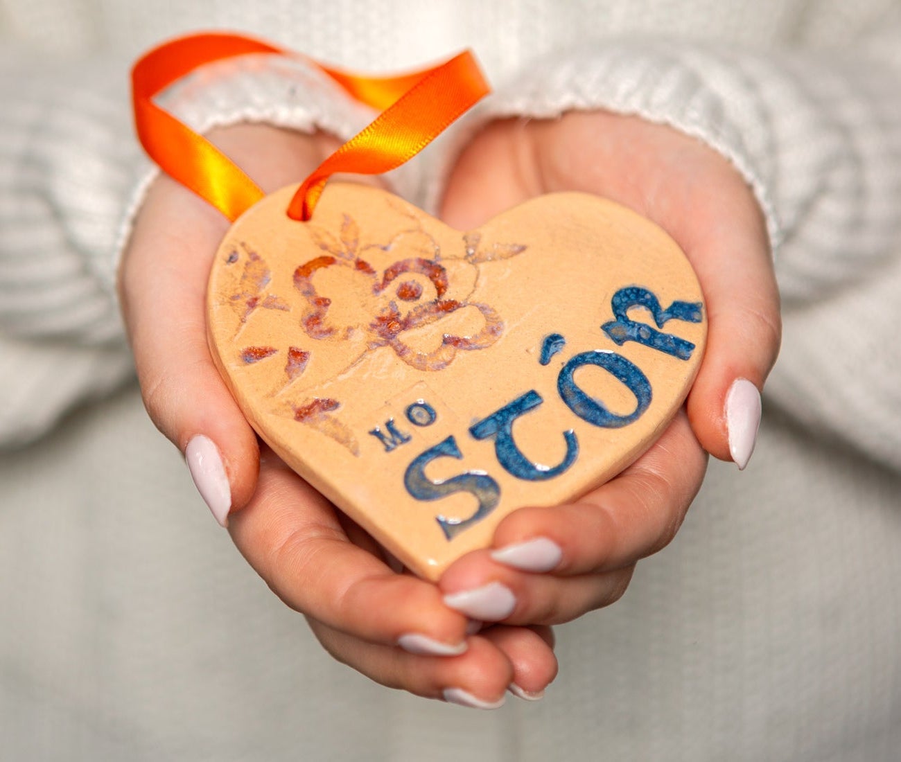 A lady's hands holding a clay heart engraved with Irish text