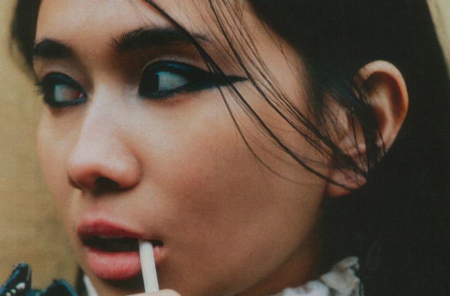 Close up view of a woman's face with black lined eyes, looking away to her right.