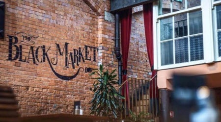 Exposed brick wall with The Black Market sign red velvet curtains and a staircase leading to an upper level