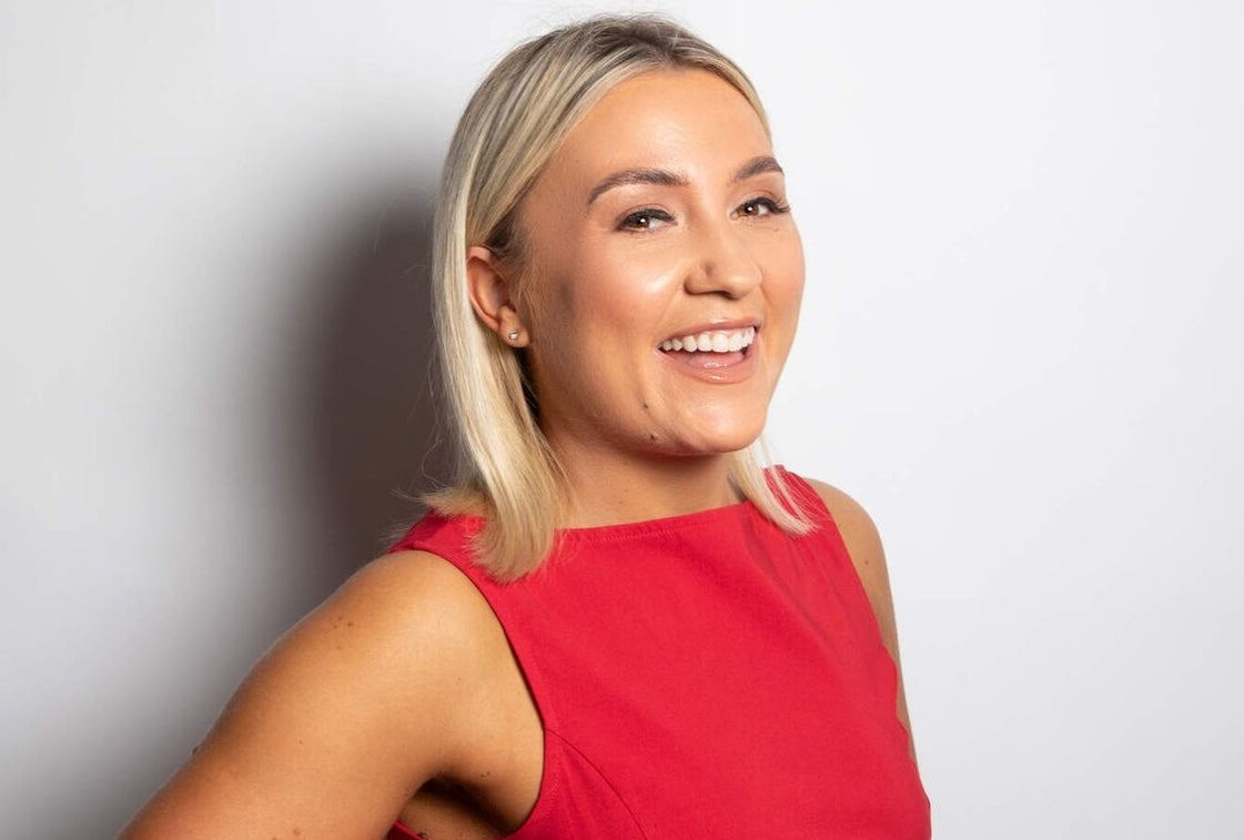 Enya Martin, a smiling woman in a red dress against a plain, light background.