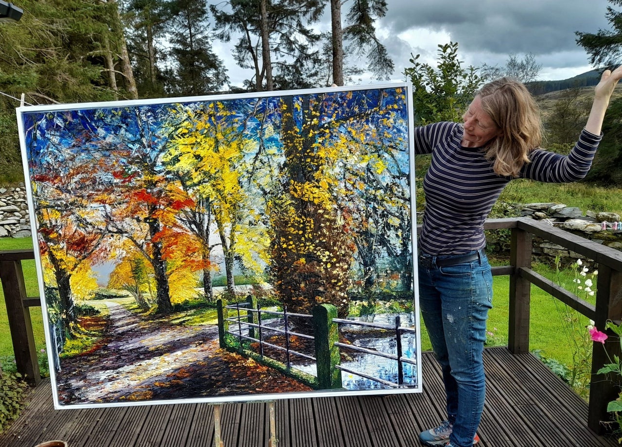 An artist standing outside displaying her oil painting