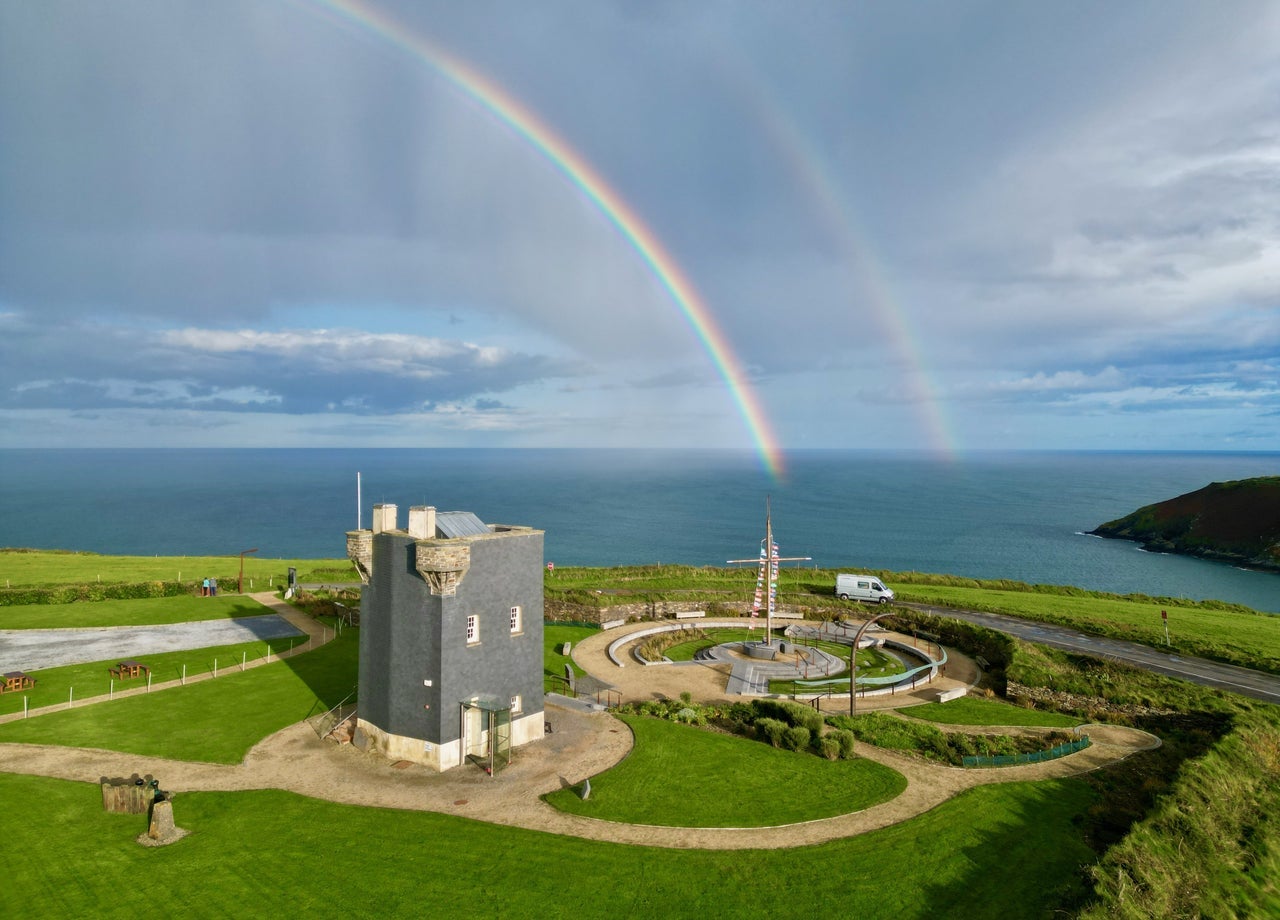A signal tower beside the coast with a double rainbow in the sky