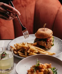 A gourmet style burger with fries on the side and a cocktail