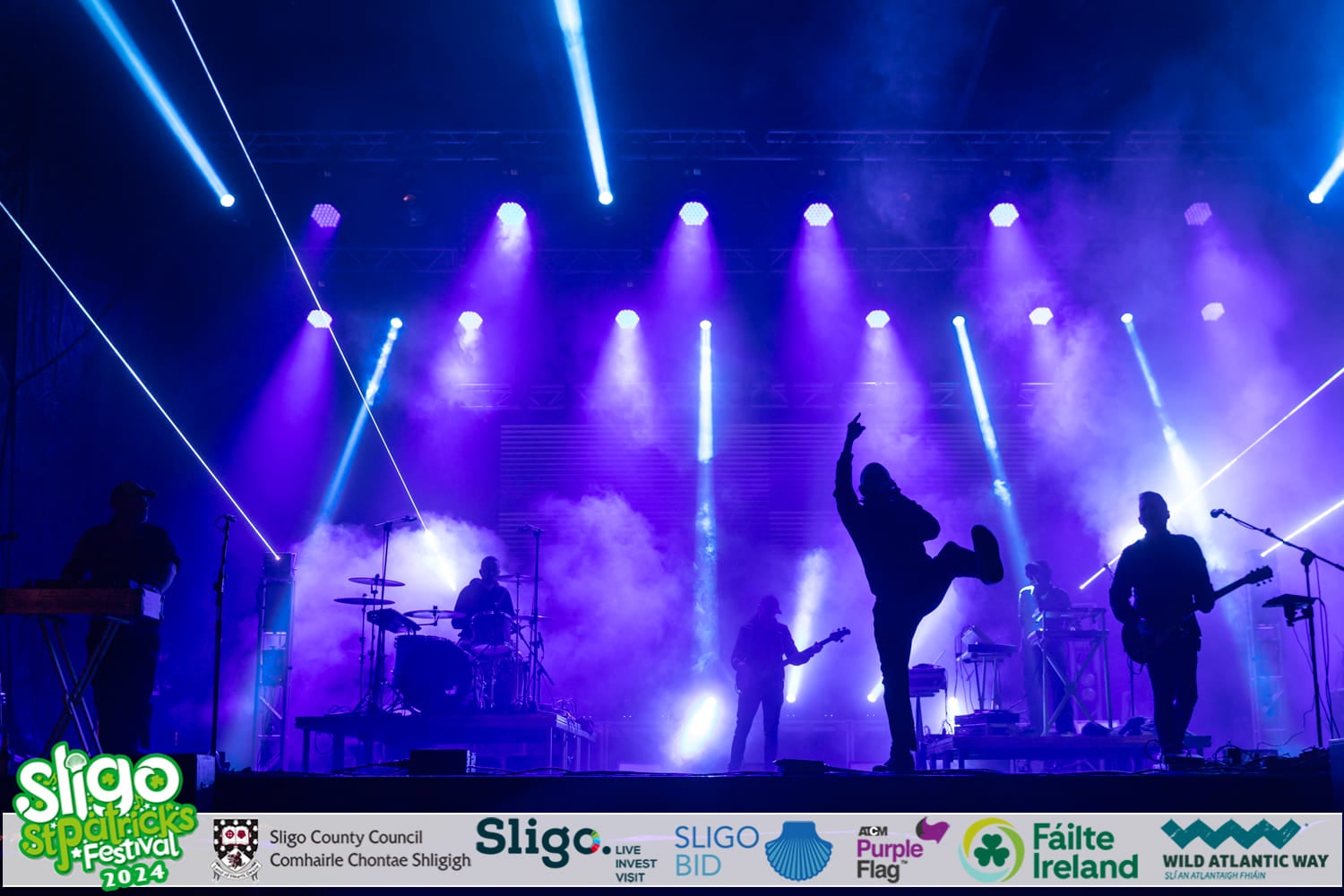 A stage with white spotlights and performers in silhouette.