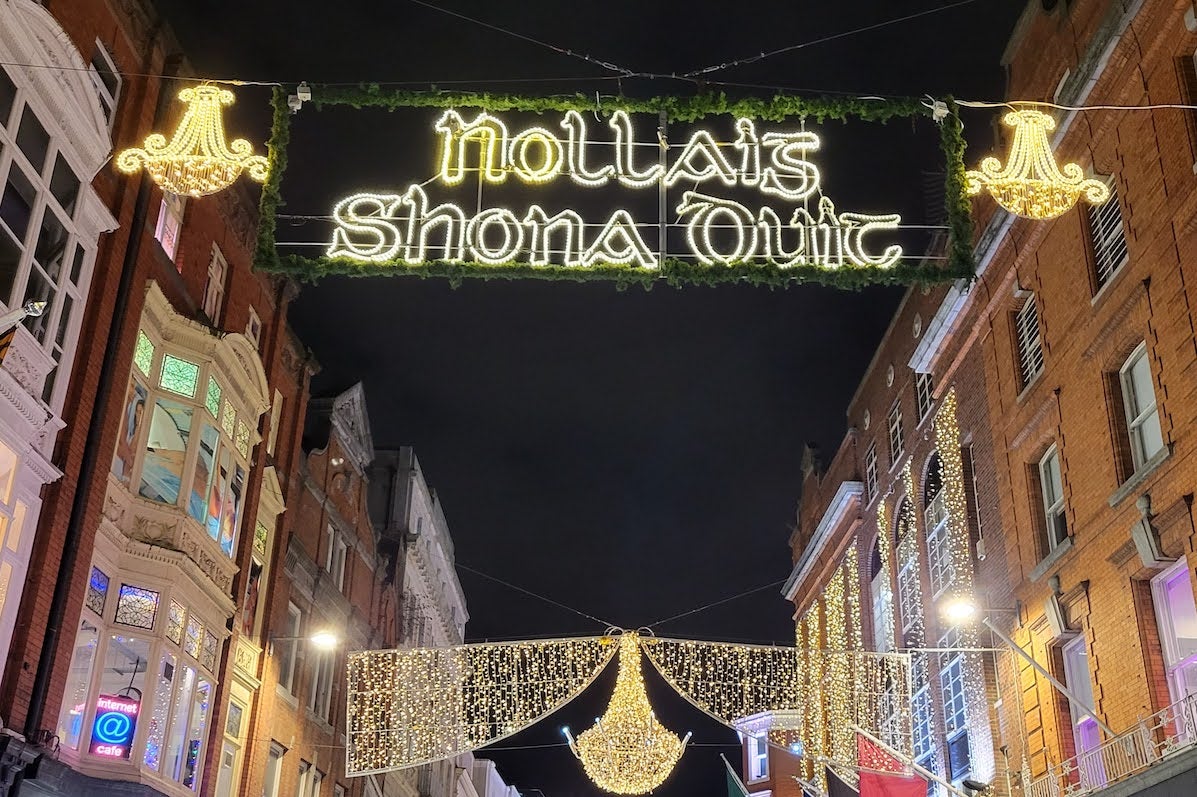 Looking up at buildings in a street at night with yellow christmas lights across the between them.