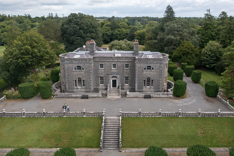 An old, large grey house set in parkland with trees.