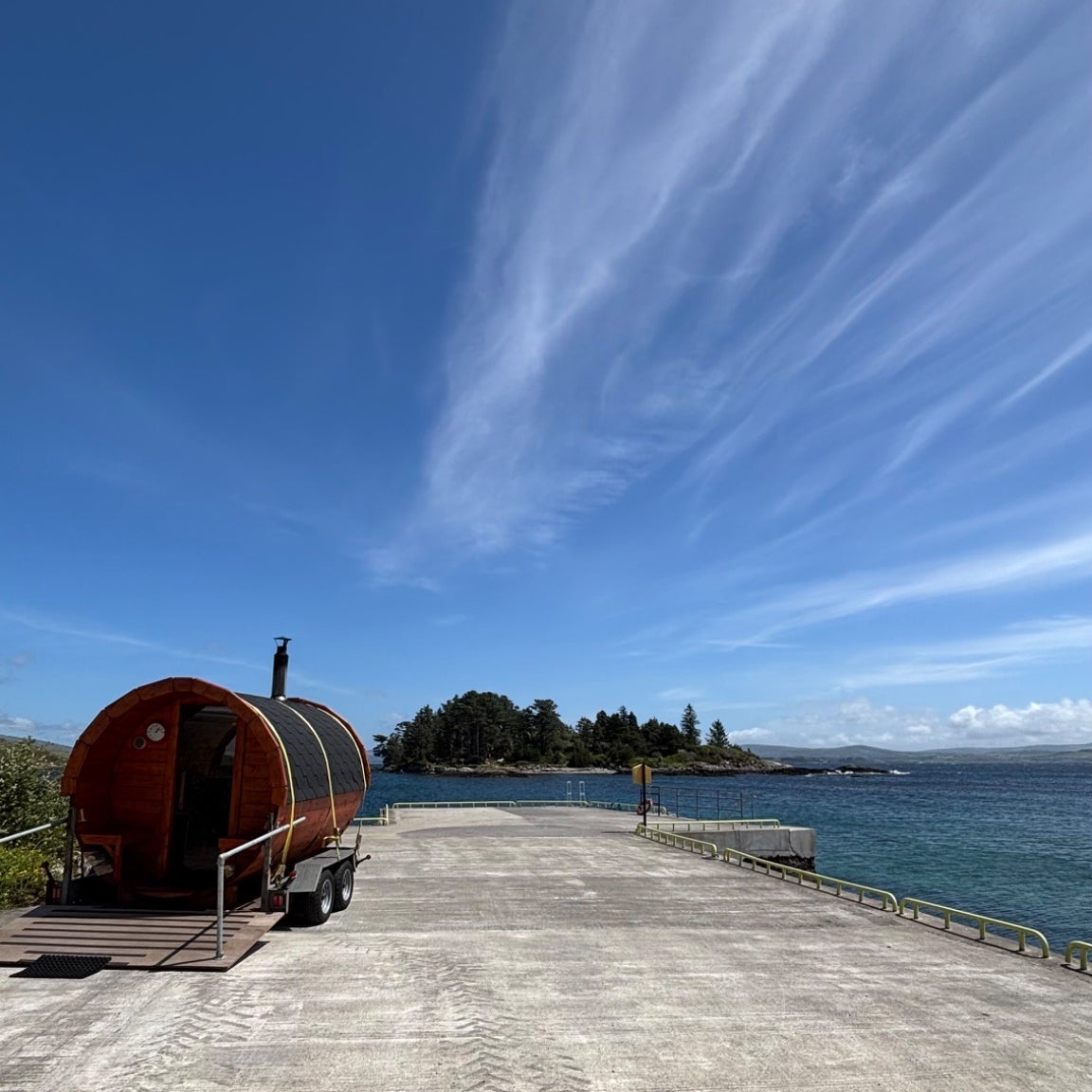 Mobile sauna unit on a pier with an island close by and blue skies overhead