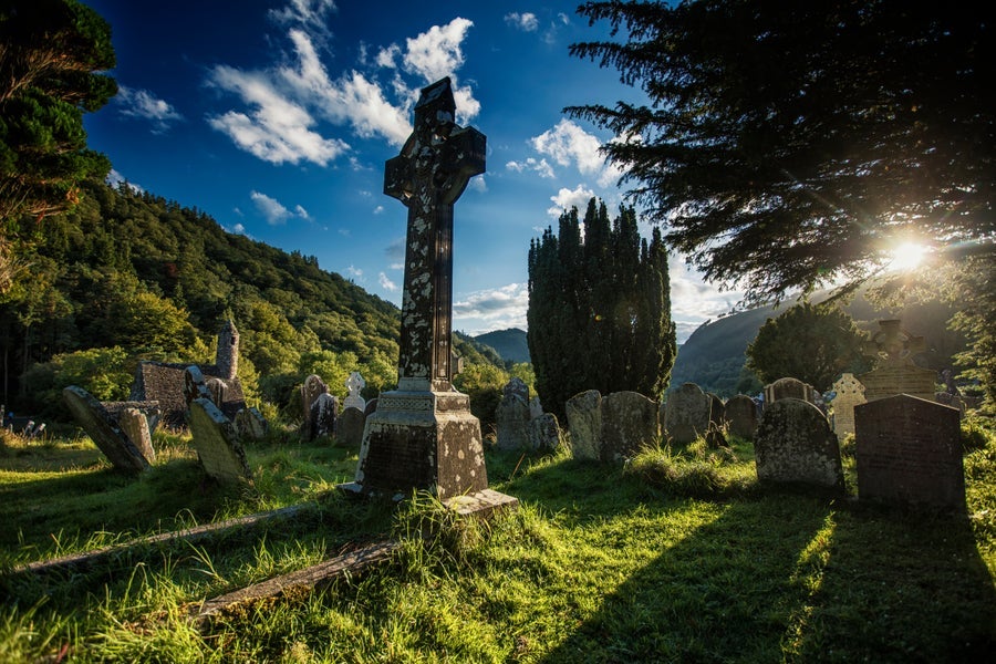 A stone high cross in a grassy cemetery under a blue sky