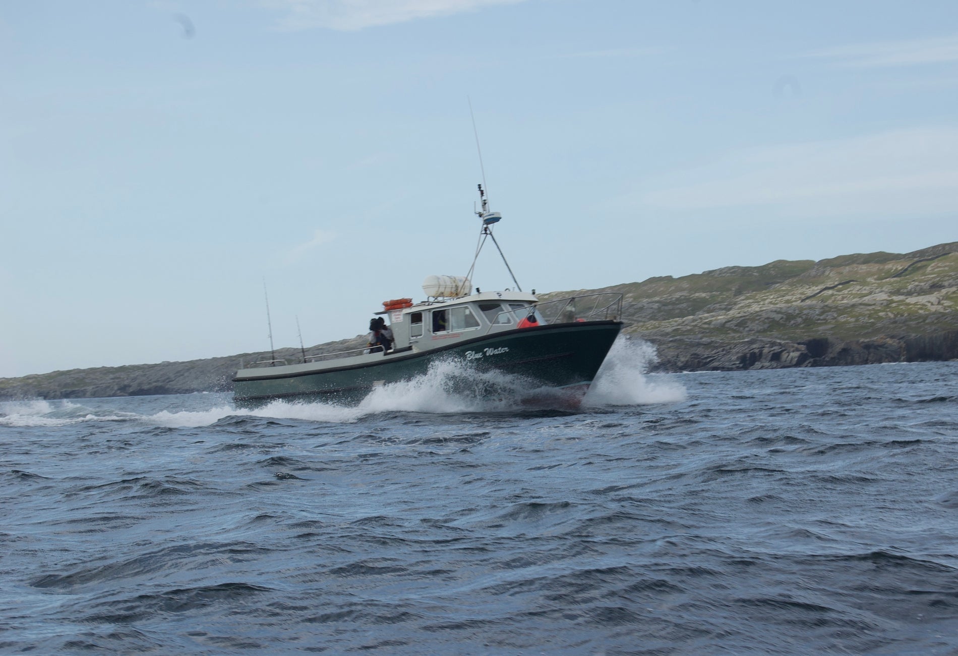 Fishing trawler at sea in rough waters with green hills to the right