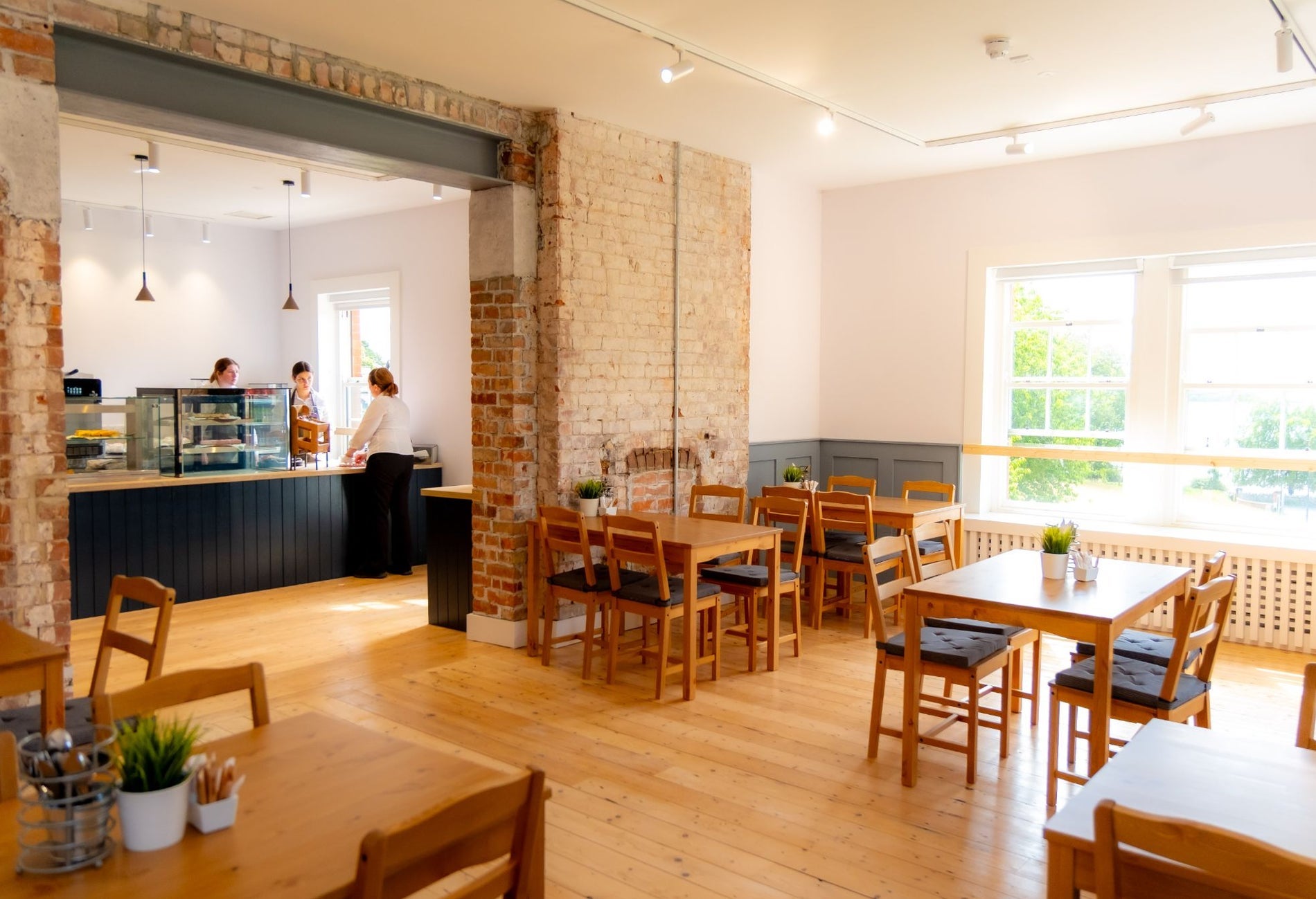 Bright café interior with wooden tables, exposed brick and a counter with staff serving customers
