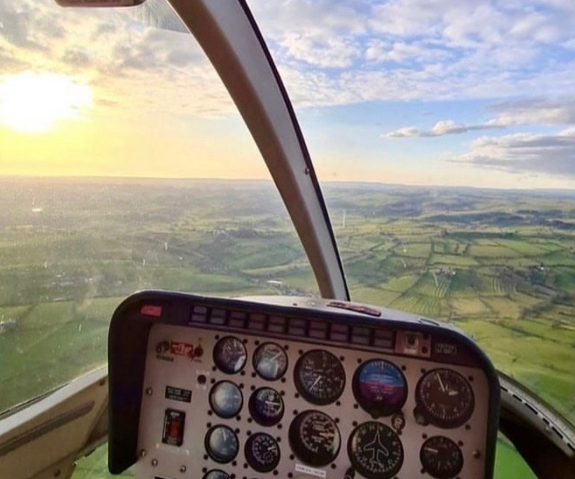 An aerial image captured inside the helicopter of the green landscape below with the sun shining