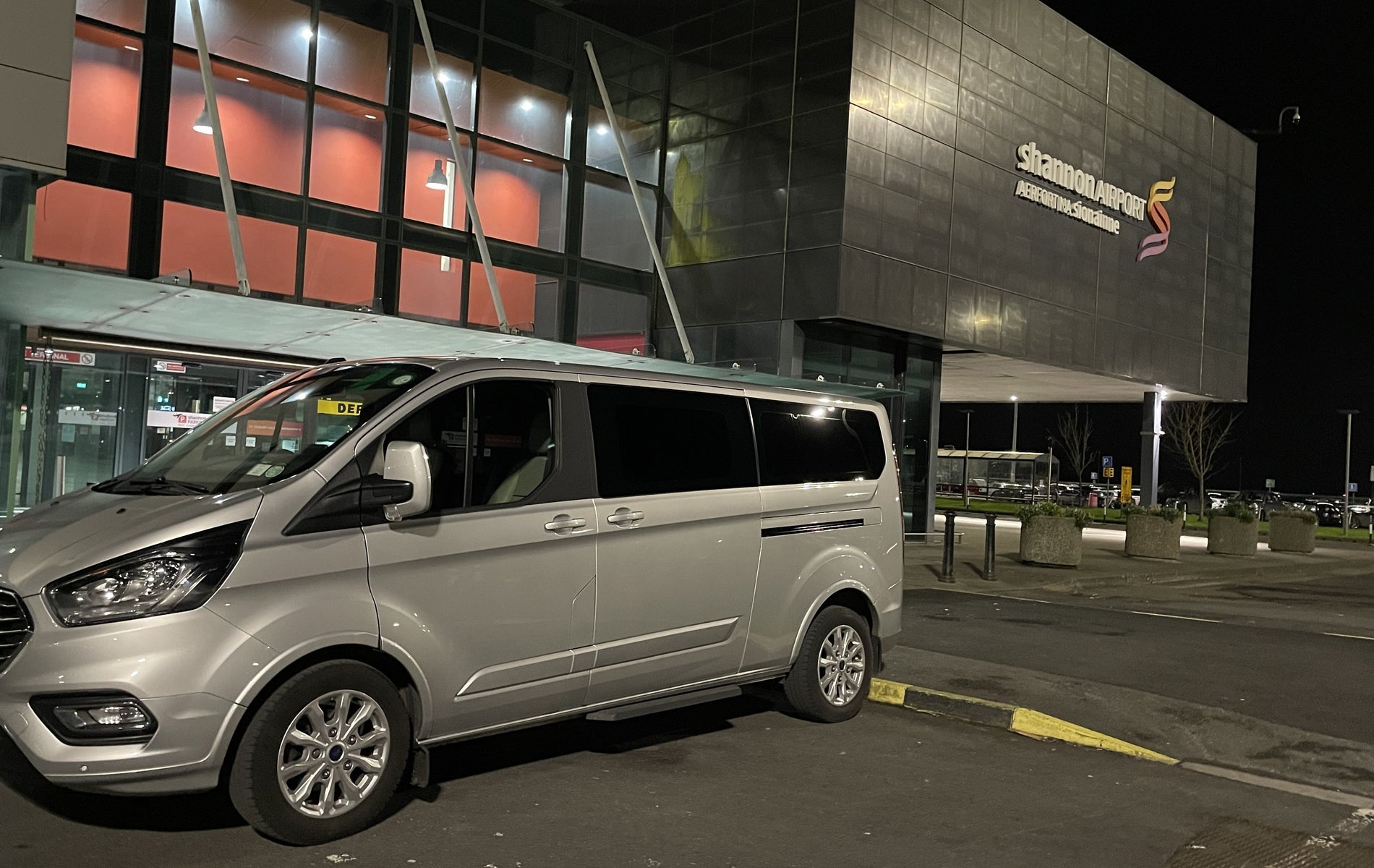 Silver mini bus parked outside an airport at night