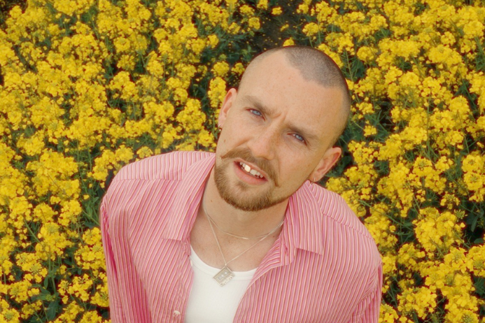 A man is looking upwards towards camera, in pale red shirt with a background of bright yellow flowers.