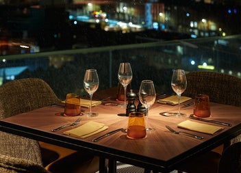 A rooftop dining table set with wine glasses and cutlery overlooking the city skyline at night