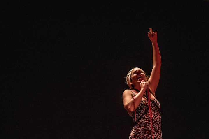 Dark stage with person holding a mic with the other hand up in the air.