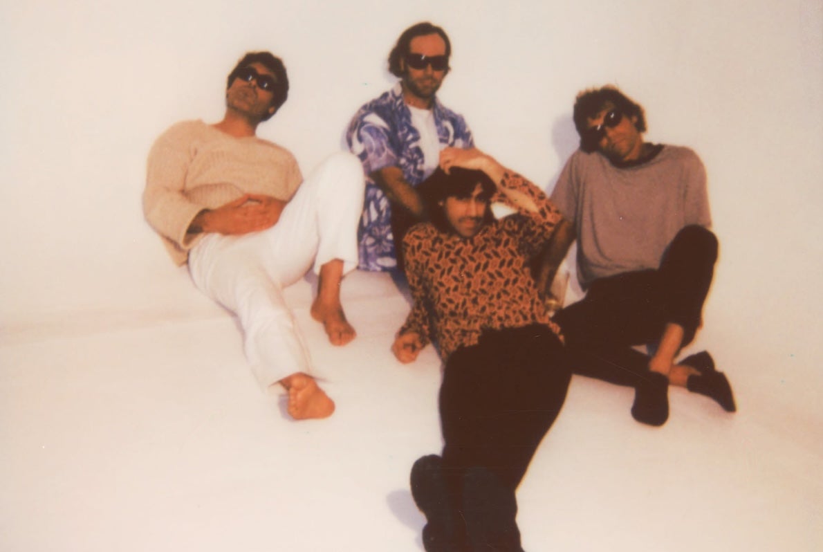 Slightly blurry photo of 4 men lounging on an off white floor and wall.