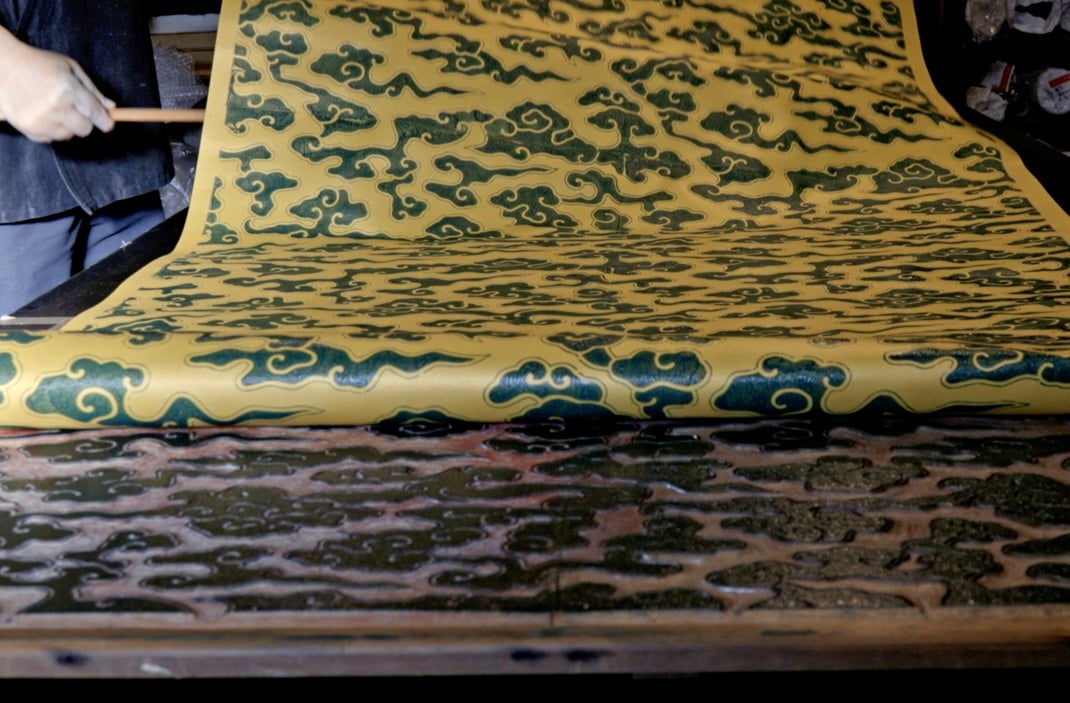 A long strip of patterned paper being rolled up from the print blocks