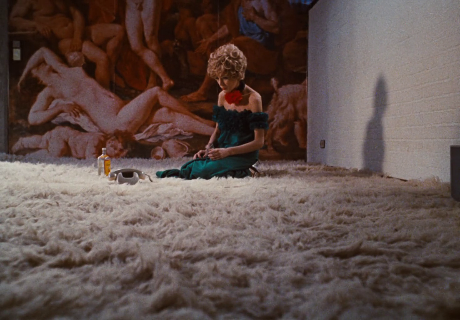 A woman in a dress is kneeling on a carpet next to a phone and a bottle.
