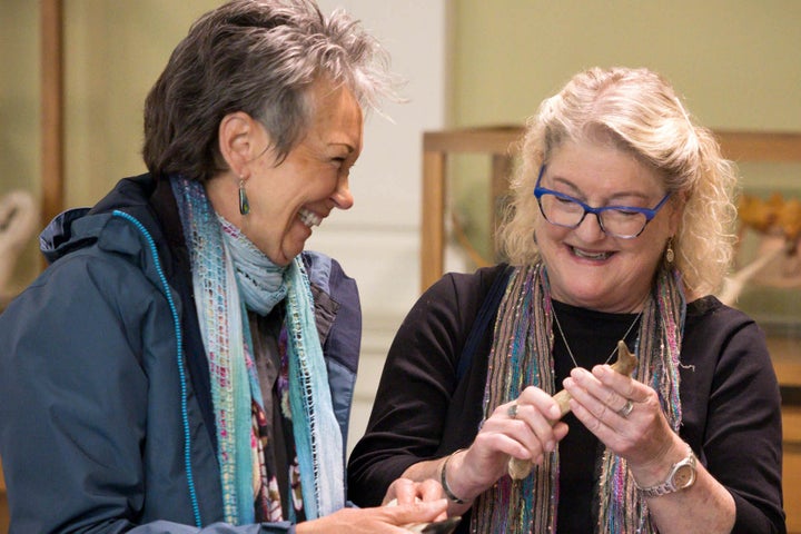 2 women laughing, both holding small objects, display cabinets in the background.