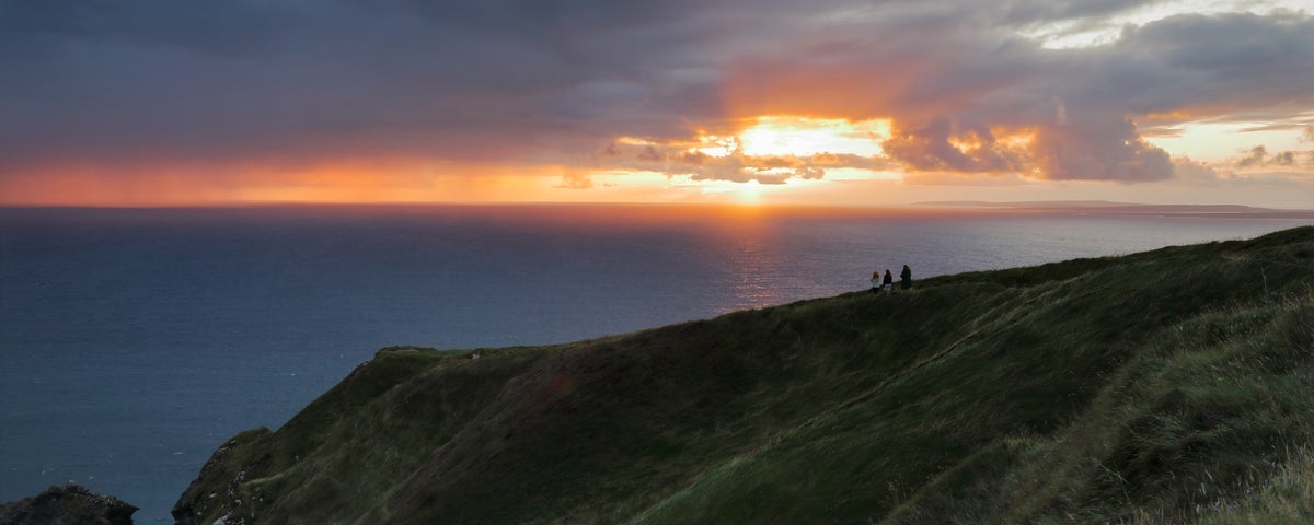 People stand on a cliff area looking out at a sunset