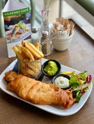 Basket of chips with a piece of battered fish and sides on a while rectangular plate
