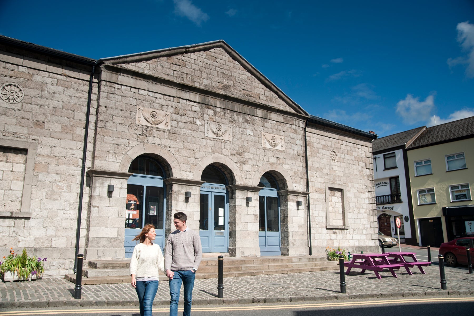 Two people walking along a street by a historic building