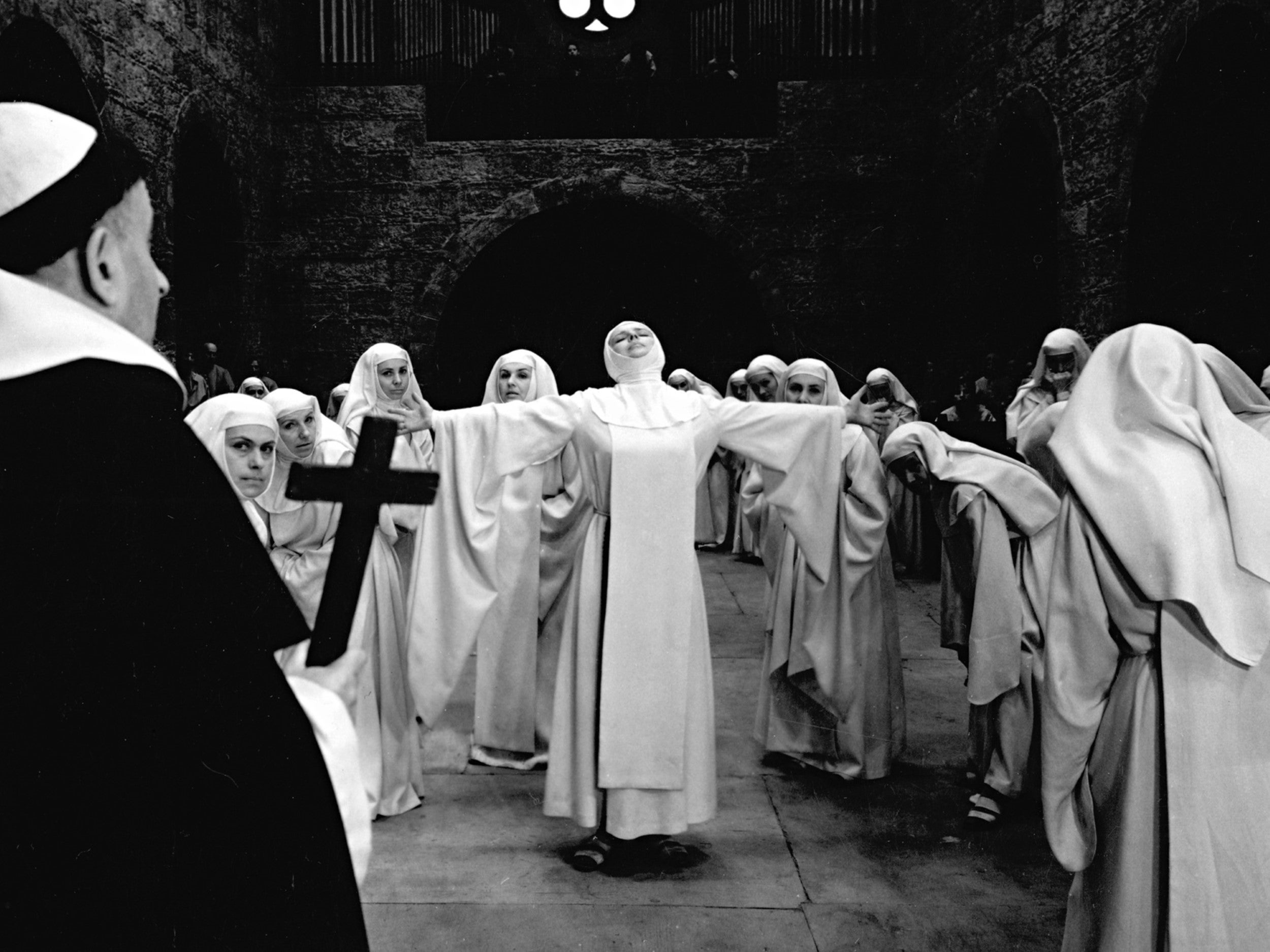 Several nuns in white habits are grouped around one with her arms outstretched.