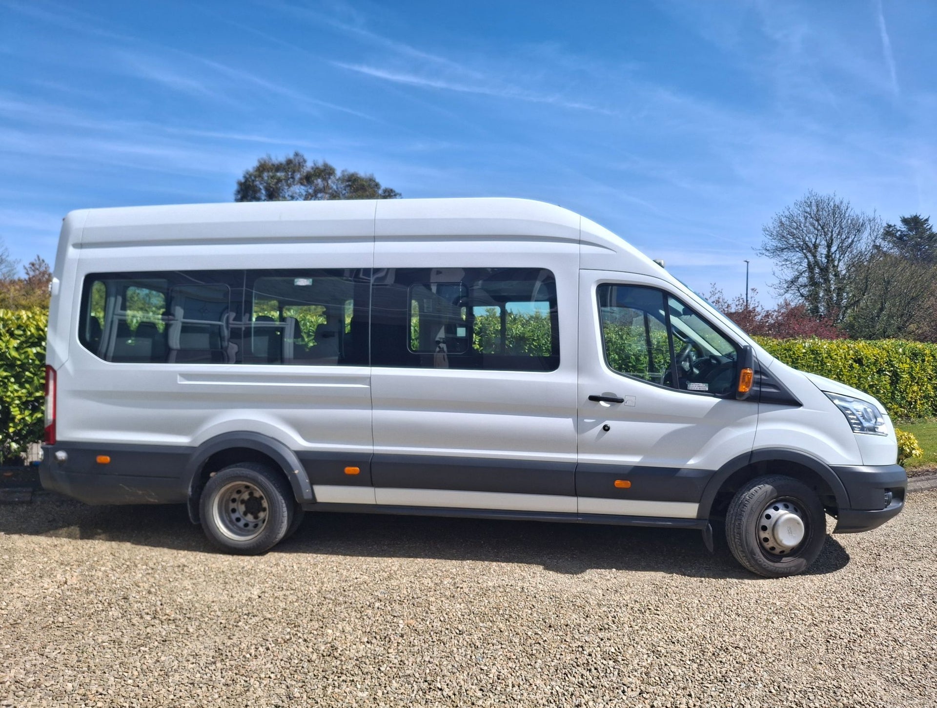 Side view of a white minibus parked on gravel with a blue sky in the background