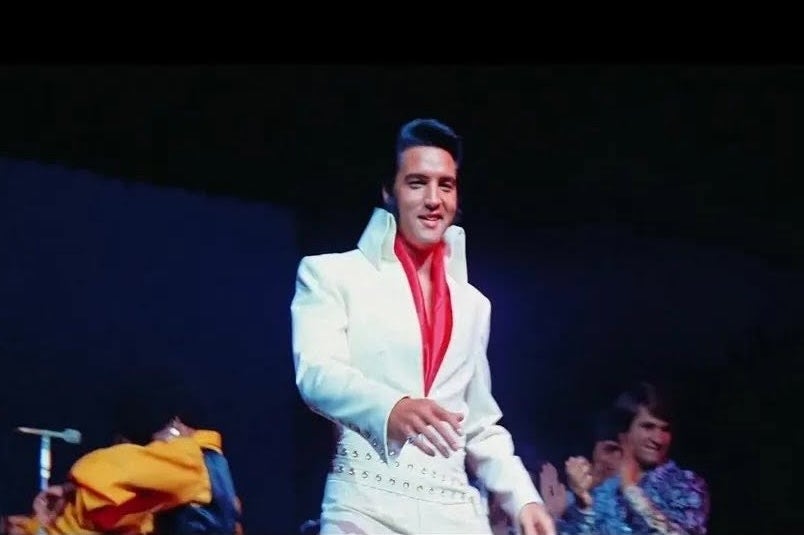 EPiC - Elvis Presley in Concert, slightly blurry photo of smiling man in white suit on black background.