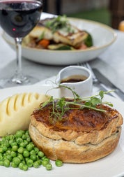 A pie served with peas mash potatoes and a glass of red wine