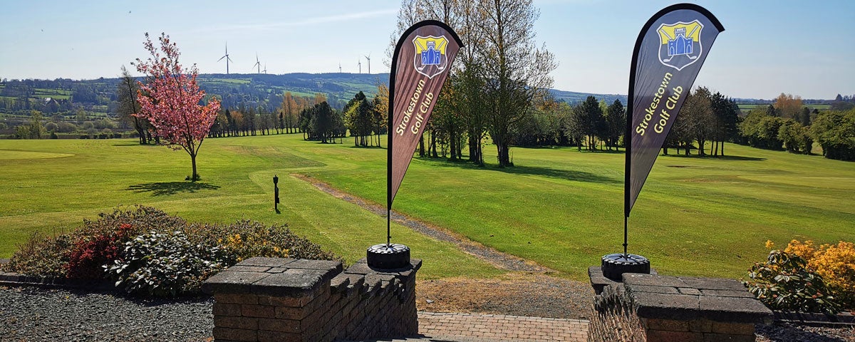 Image of two banner flags at the entrance to Strokestown Golf club with golf course in the background