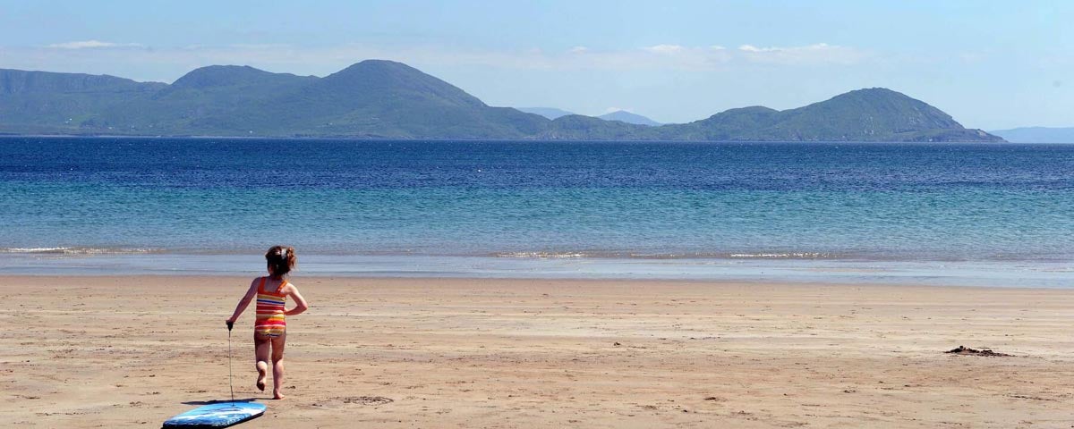 Child on Ballinskelligs Beach pulling surf board 