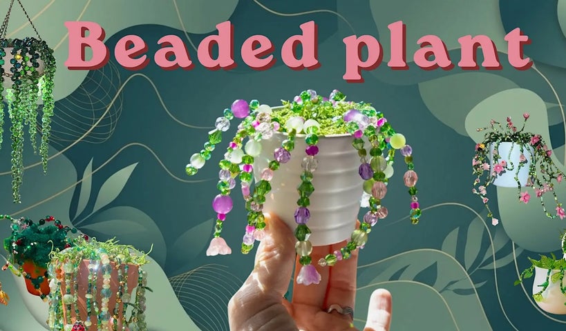 A hand holding up a small white pot with different coloured beaded strings trailing down the sides.