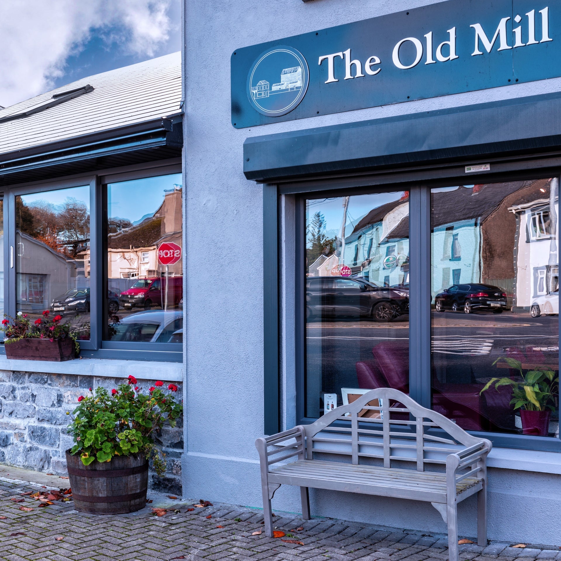 Blue building on a footpath with a seat outside and cars reflected in the windows