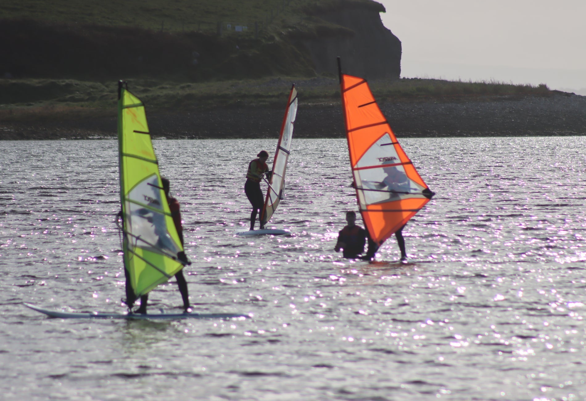 People surfing at sea with yellow and orange sails