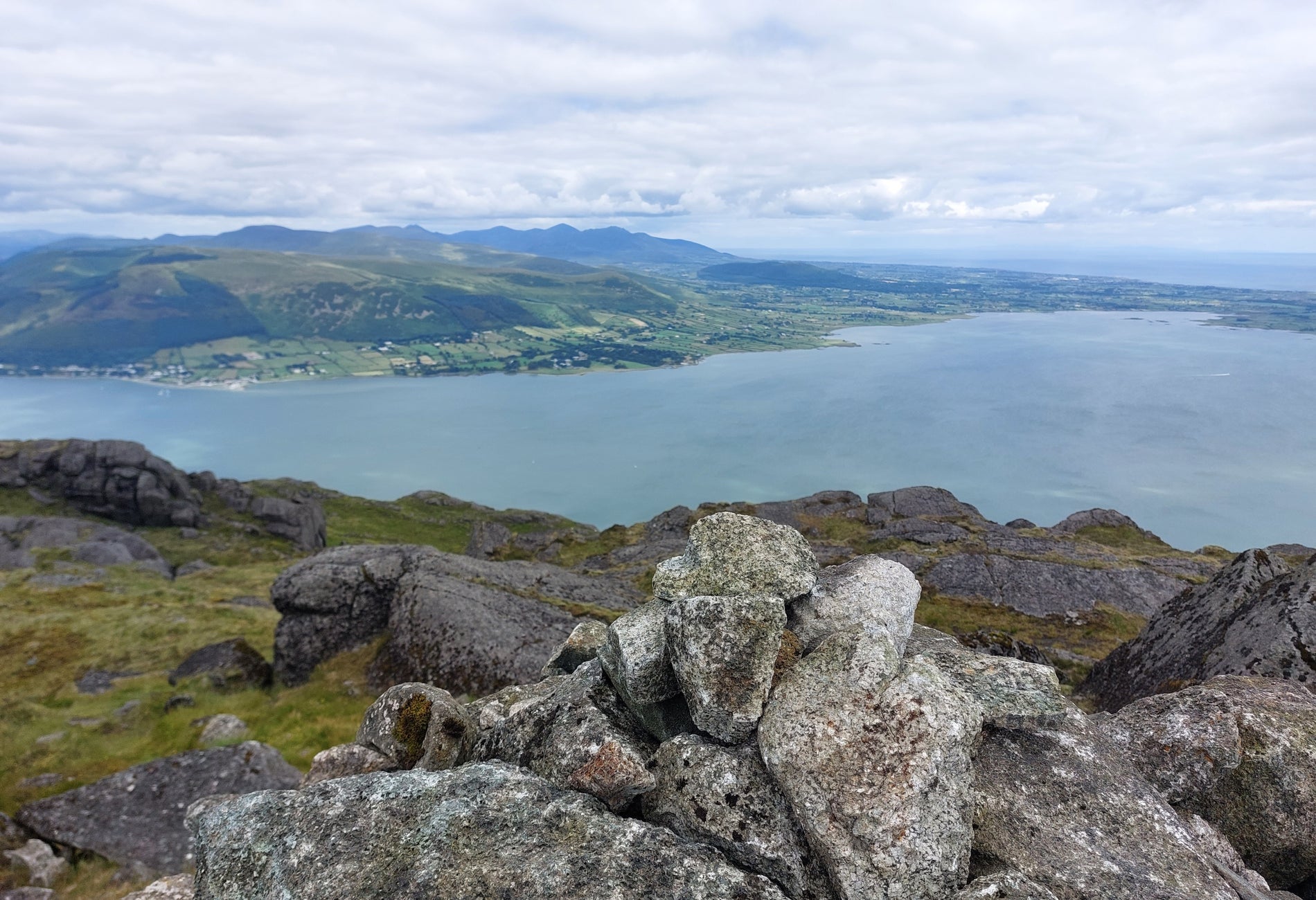 View from above a body of water taken from behind big stones with green fields in the distance
