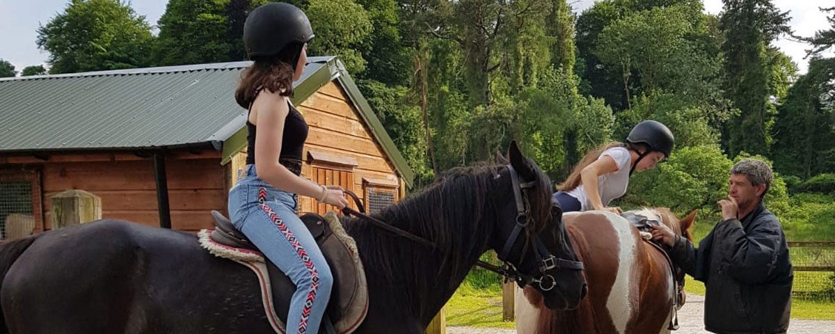 Two people on horseback and an instructor on foot speaking to them