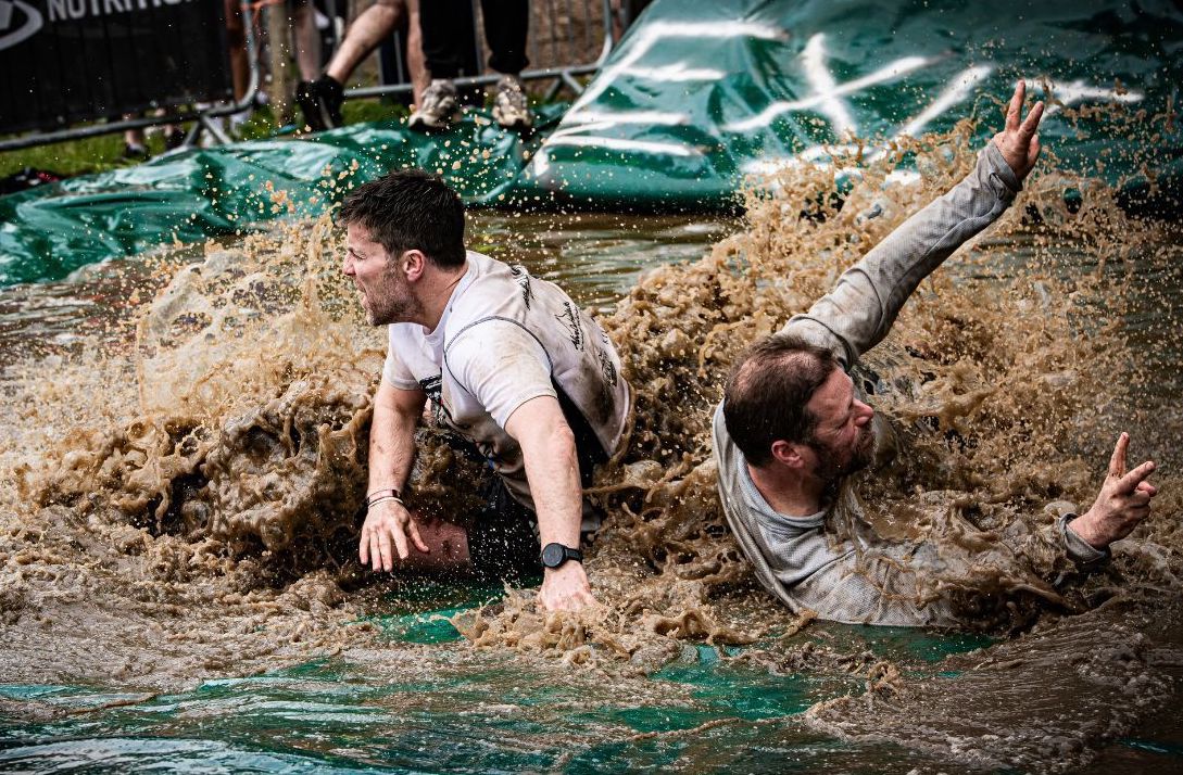 2 men are splashing through man made area of muddy water