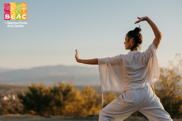 A woman dressed in white in a movement pose with arms outstretched outdoors with distant view.