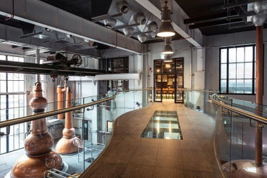 An elevated walk way with an aerial view of copper stills in a distillery