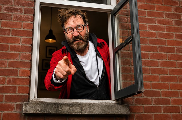 An angry looking man pointing a finger is at a small open window